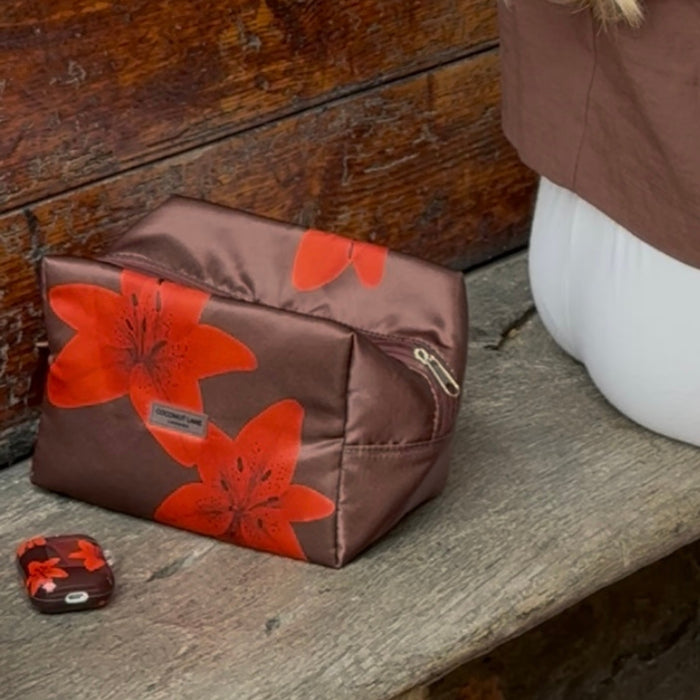Brown bag with red flower prints and a Cinnamon Lily Coconut Lane AirPods case beside someone in white pants.