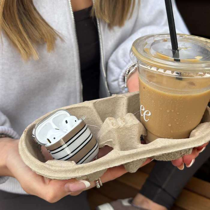Woman holding iced coffee and two Coconut Lane Airpods cases, one with retro stripes, in a drink carrier.