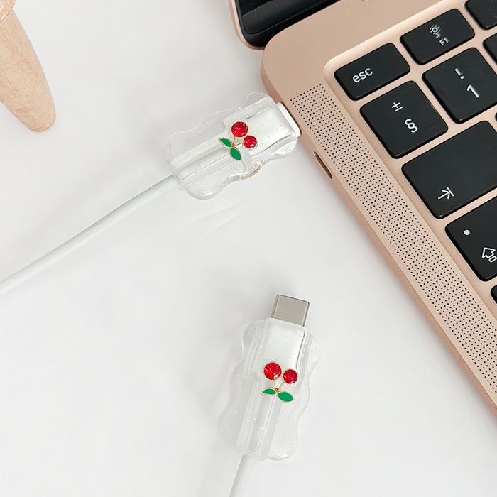White charging cables with cherry-patterned cable charms connect to a rose gold laptop.