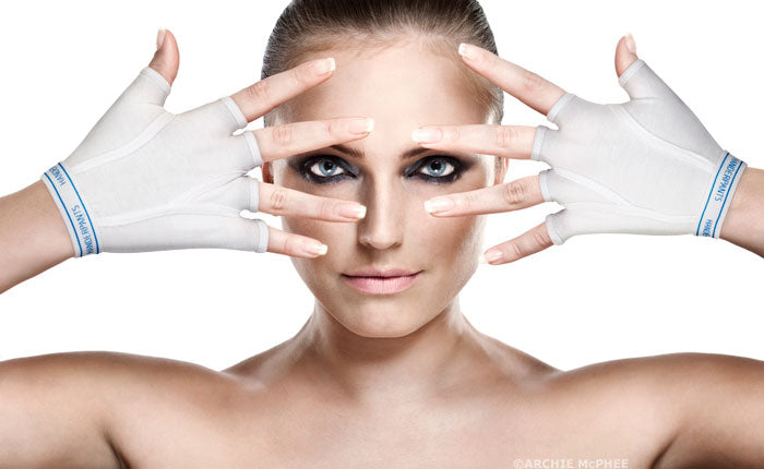 A striking woman with bold eye makeup poses elegantly, her hands framing her face while she wears a pair of white Handerpants.