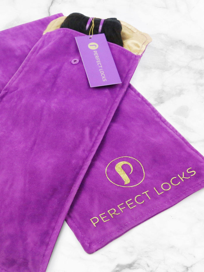 A purple suede pouch with the Perfect Locks gold circular logo and a matching tag holds Relaxed Straight Clip-In Ponytail Extensions, displayed on a white marble surface.