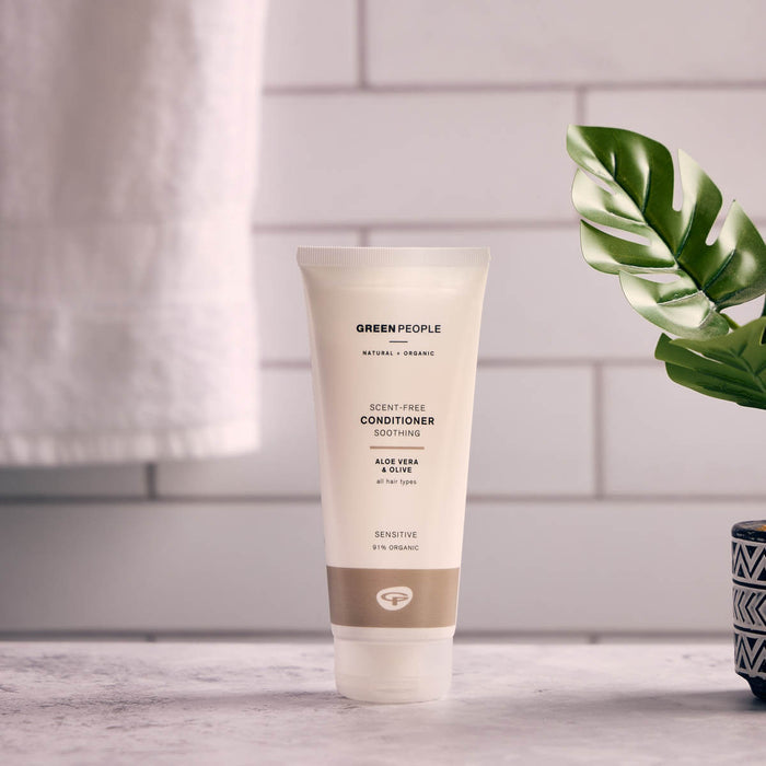 Tube of Green People conditioner on a bathroom counter with a leafy plant in the background.