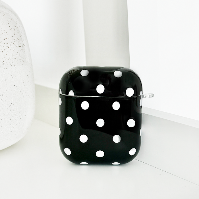 Coconut Lane black polka dot AirPods case next to a textured white object on a clean white surface.