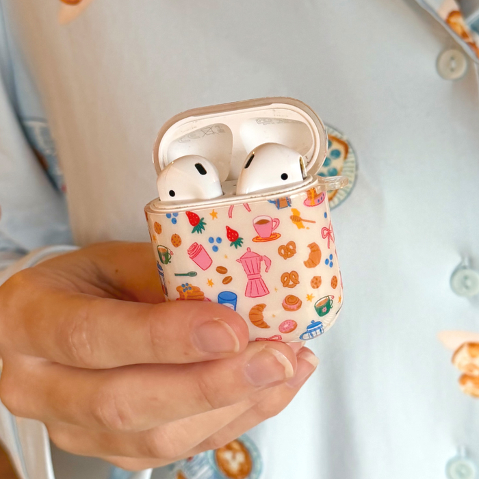 Hand holding Coconut Lane AirPods case with a vibrant, breakfast-themed pattern in multiple bright colors.