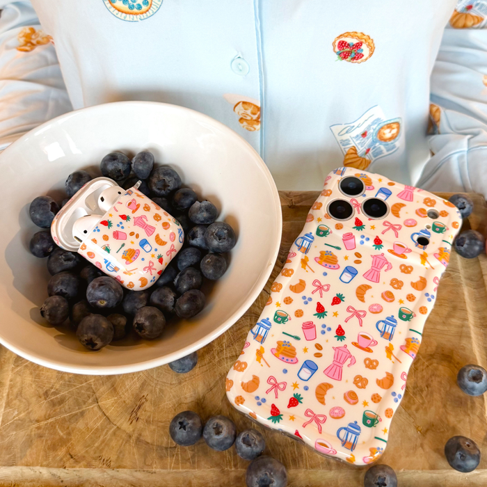 Blueberry-patterned AirPods case by Coconut Lane in a bowl of blueberries; matching bakery-themed items nearby.