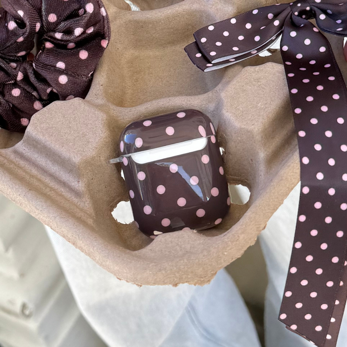 Brown polka dot Coconut Lane AirPods case in carton beside matching scrunchie and ribbon.