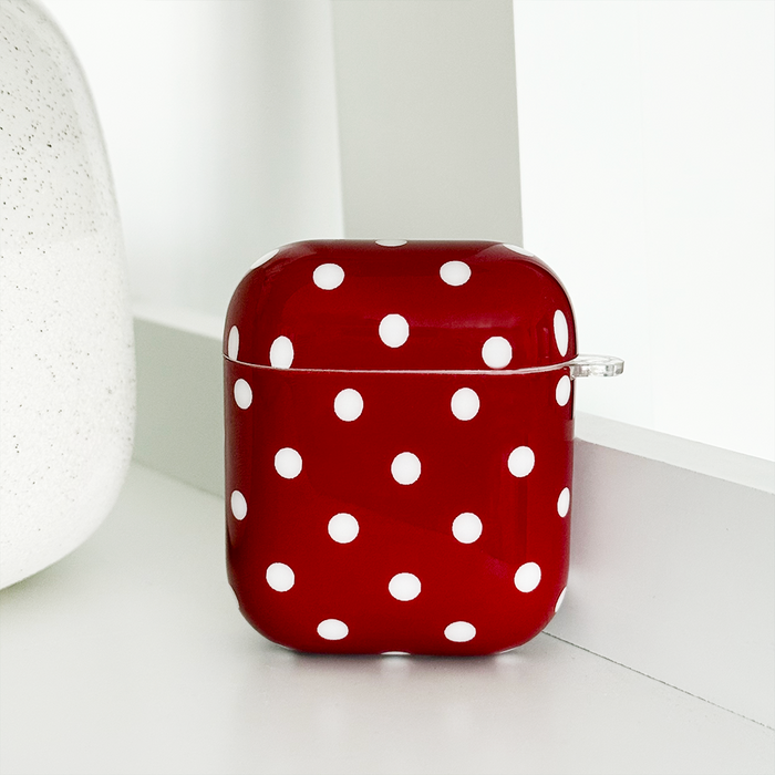 Burgundy polka dot Coconut Lane Airpods case on a white surface beside a light, textured object.