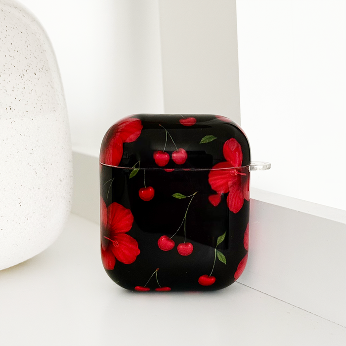 Cherry Hibiscus patterned Coconut Lane AirPods case on a white shelf beside a white speckled object.