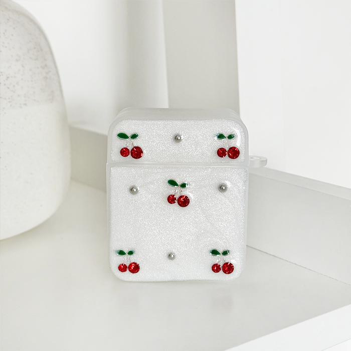 Glittery white AirPods case with red cherries and silver studs on a white surface.