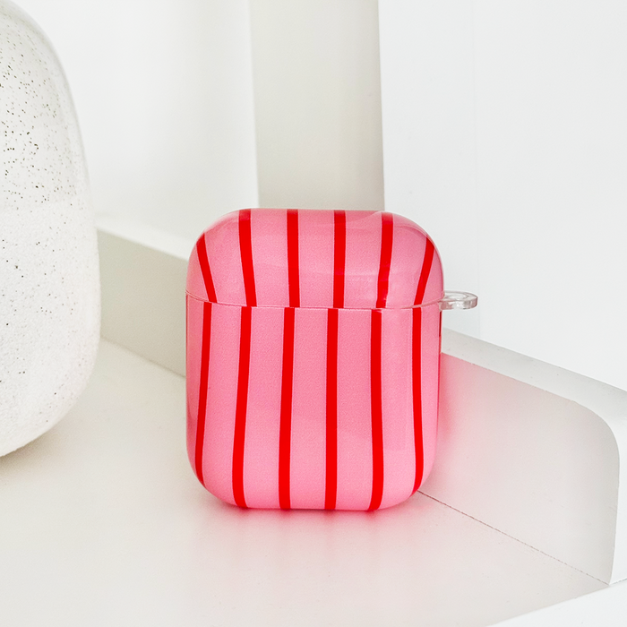 Red and pink striped Airpods case with cherry pattern on a white shelf next to a textured decor piece.