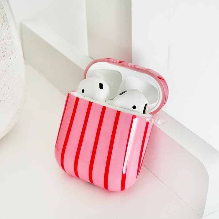 Coconut Lane Cherry Stripes AirPods case with white earbuds on a white surface near a wall.