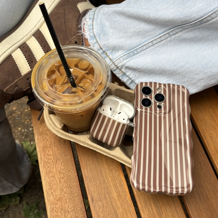 Striped phone case, Coconut Lane Chestnut Stripes AirPods case, iced coffee, white sneakers, and blue jeans.