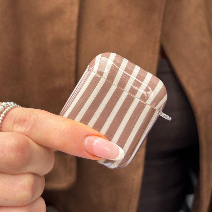 Hand holding Coconut Lane AirPods case with chestnut and white stripes, shown against a brown jacket background.