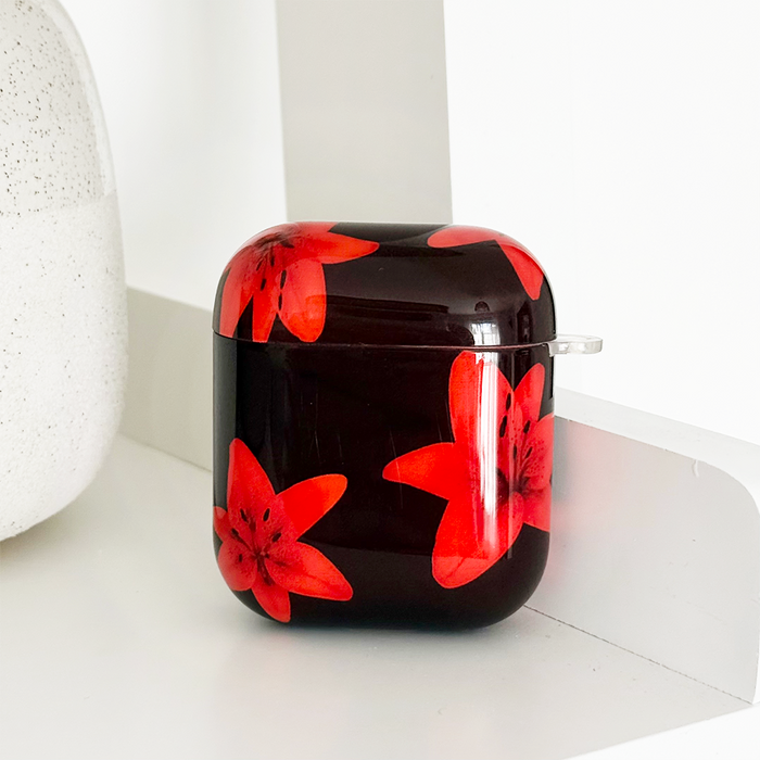 Coconut Lane AirPods case in Cinnamon Lily pattern with red flowers, displayed on a white shelf.