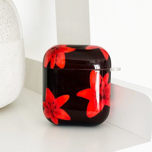 Coconut Lane AirPods case in Cinnamon Lily pattern with red flowers, displayed on a white shelf.