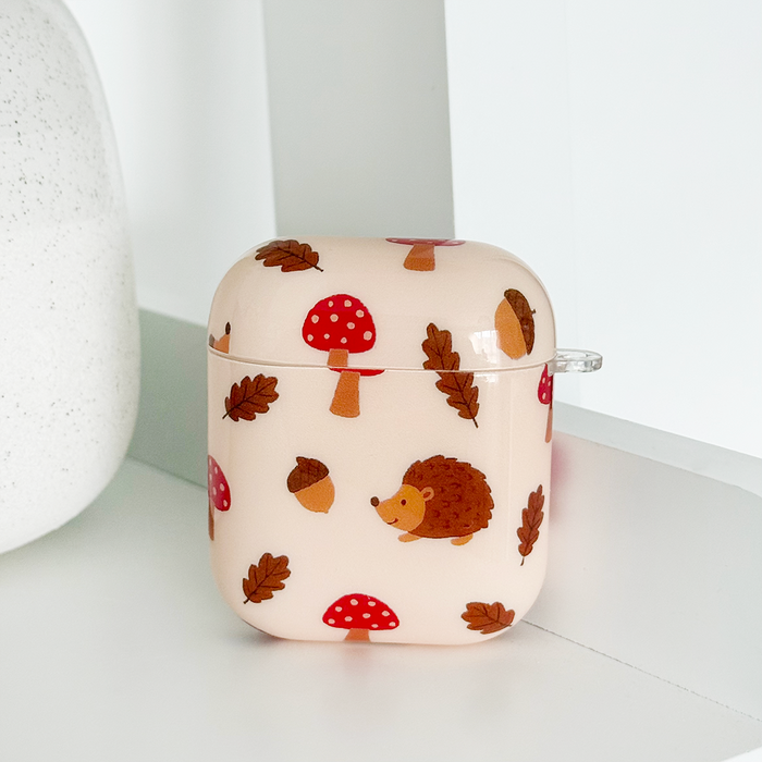 Coconut Lane Airpods case with a forest pattern featuring hedgehogs, mushrooms, and leaves on a light background.