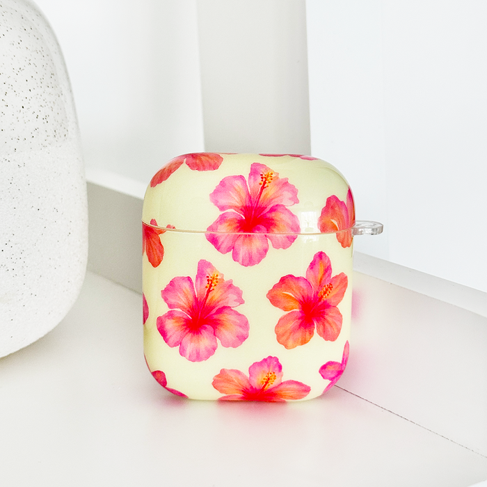 Butter yellow AirPods case with pink hibiscus floral pattern, displayed on a white shelf.