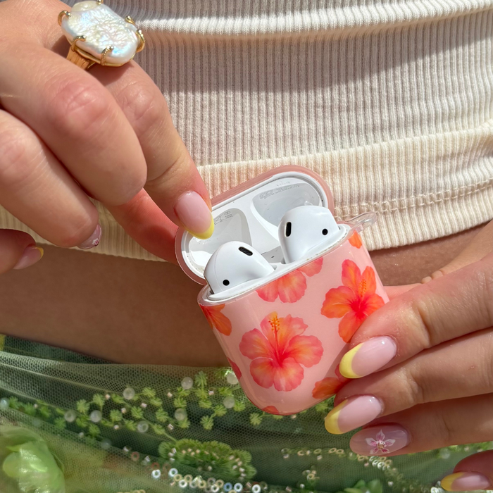 Coconut Lane Island Girl Pink Hibiscus AirPods case held in hand with pastel nails, pearl ring, and ribbed top.