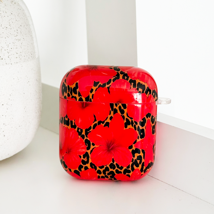 Red floral print Coconut Lane Airpods case with leopard accents displayed on a white shelf.