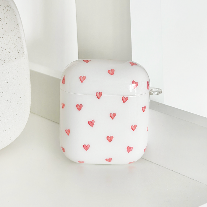 White Coconut Lane Airpods case with a pattern of small red hearts.