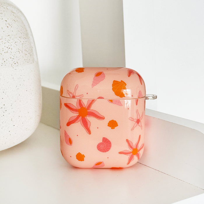 Coconut Lane Airpods case with orange and pink floral leaf pattern, displayed on a white shelf.