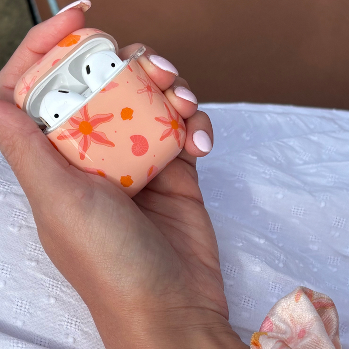 Peachy Beach Coconut Lane Airpods case with white earbuds held in a hand with light pink nails, white dress in background.