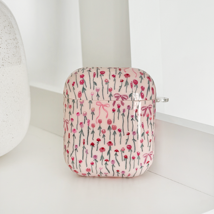 Coconut Lane Airpods case in a floral and bow pattern, pink tones, displayed on a white shelf beside a textured ornament.