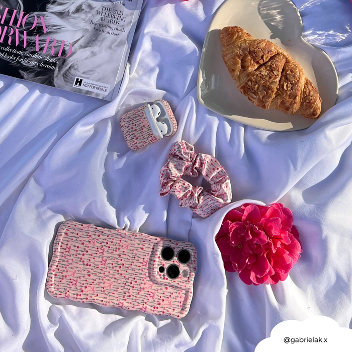 Croissant on heart-shaped plate with pink flower, floral Peony Bow AirPods case, phone, and pastel scrunchie.