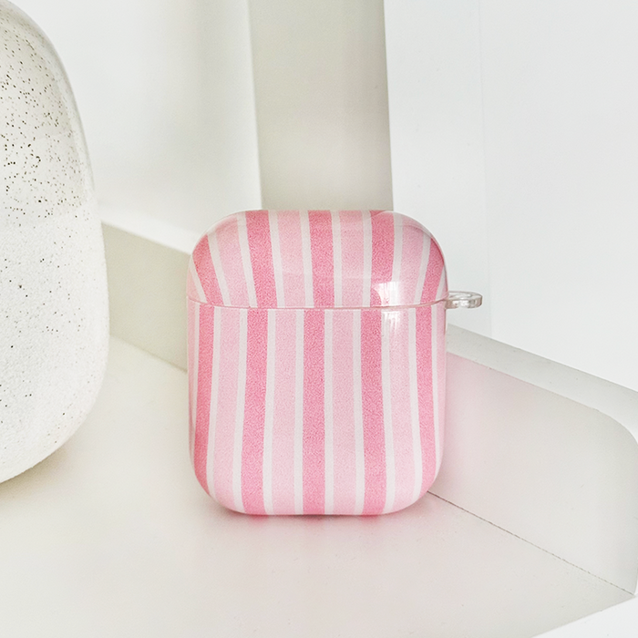 Powder Stripes AirPods Case with pink and white stripes, displayed on a white surface beside a speckled object.
