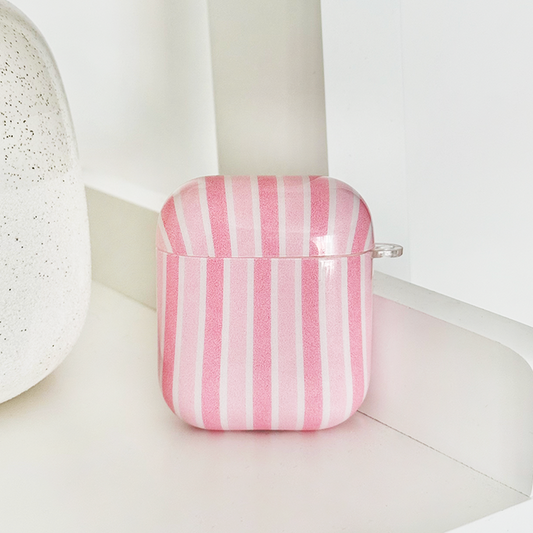 Powder Stripes AirPods Case with pink and white stripes, displayed on a white surface beside a speckled object.