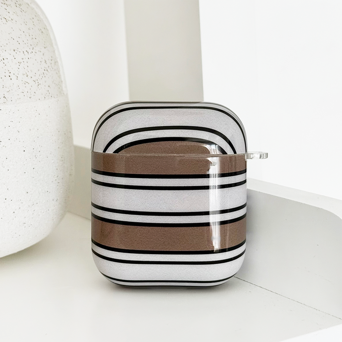 Coconut Lane AirPods case with white, brown, and black retro stripes on a white shelf next to a textured vase.