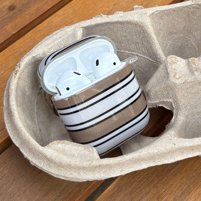 Coconut Lane AirPods case with retro stripes and AirPods placed in a beige tray on a wooden surface.