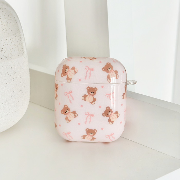 Pink Coconut Lane Airpods Case with bows, Thea Teddy design, displayed on a white shelf beside a speckled vase.