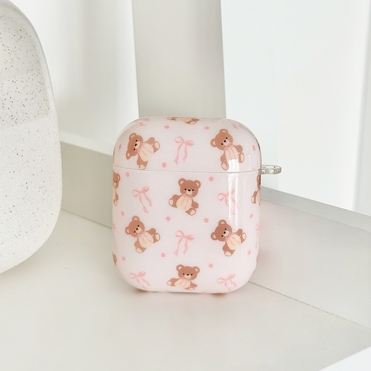 Pink Coconut Lane Airpods Case with bows, Thea Teddy design, displayed on a white shelf beside a speckled vase.