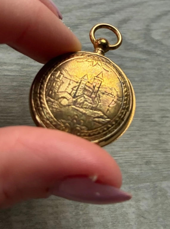 Gold pocket watch held by a hand on a gray background