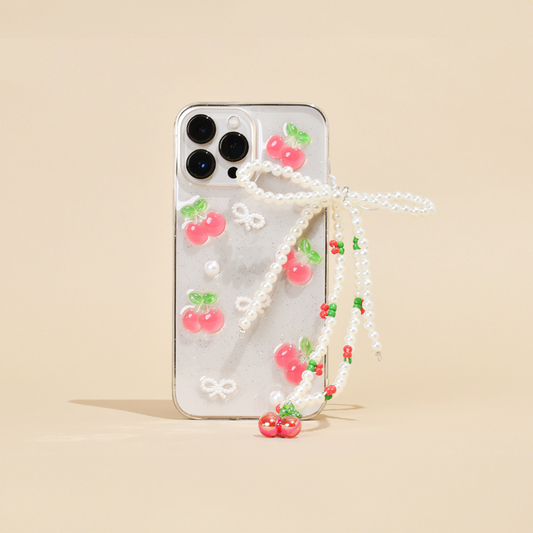 Beaded phone strap with cherry and pearl accents on a clear case with pink cherries, set against a beige background.