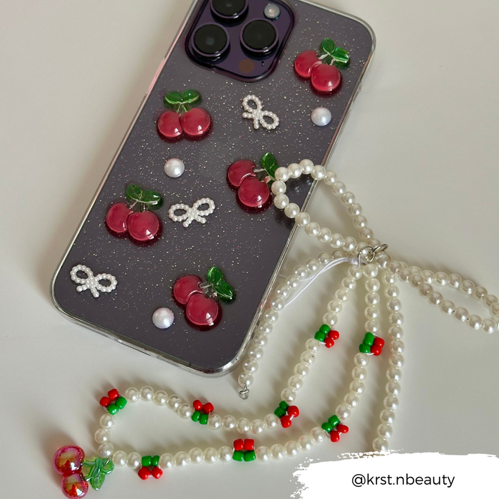 Phone with cherry, pearl, and bow decorations, featuring a Coconut Lane Cherry Pearl beaded phone strap with playful charms.