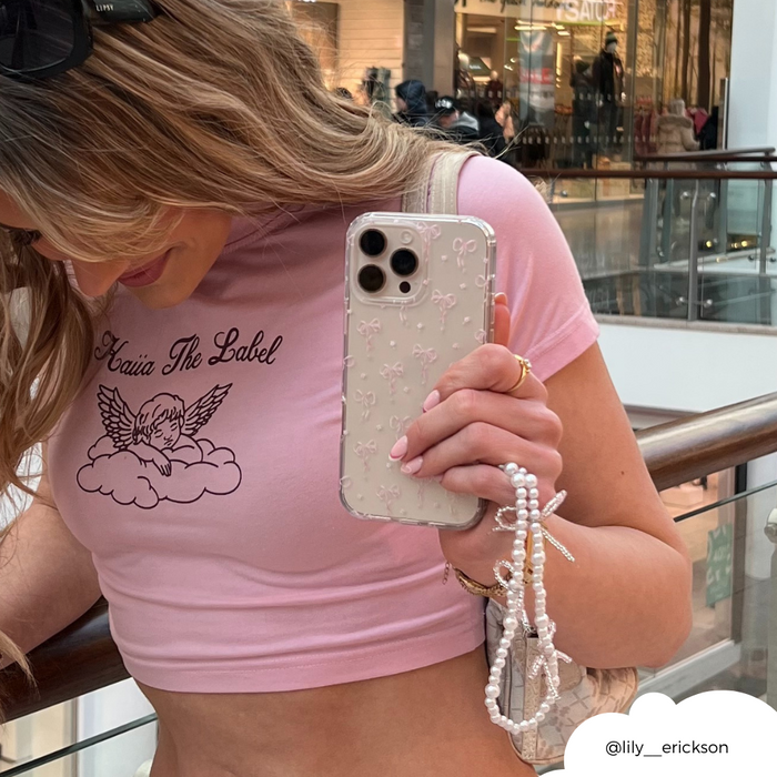 Woman in a pink crop top holds a phone with a beaded phone strap featuring small pearl bows from Coconut Lane.