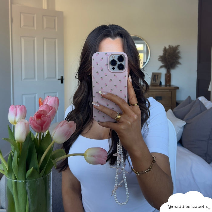 Woman wearing white top holds phone with Coconut Lane mini pearl bows beaded strap; pink tulips in foreground.