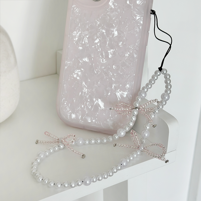 Beaded phone strap with small pearl bows and a pearlescent phone case on a white surface.
