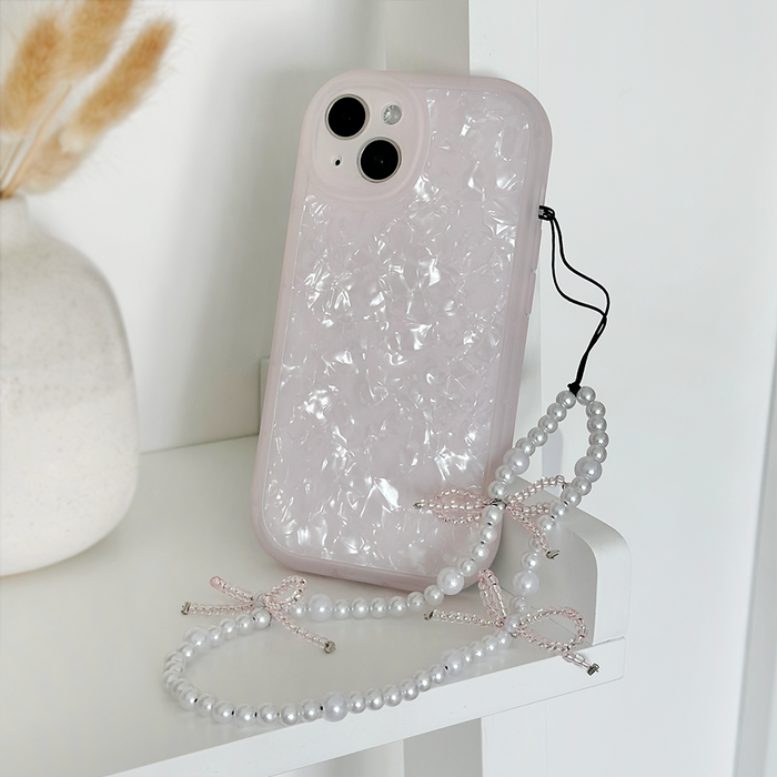 Beaded phone strap with mini pearl bows and a pearly pink case displayed on a shelf near a vase of dried grass.