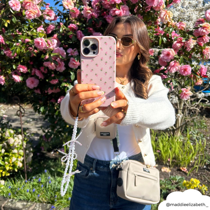 Woman with sunglasses holds pink phone featuring a Coconut Lane beaded strap with small pearl bows.