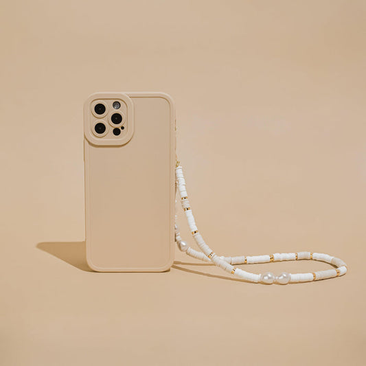 A Beaded Phone Strap in Nude & Pearl, created by Coconut Lane, adorns a beige phone case against a matching beige background. The case features a cutout for four camera lenses and is elegantly detailed with charming phone charms, complemented by white beads and small gold accents on the strap.