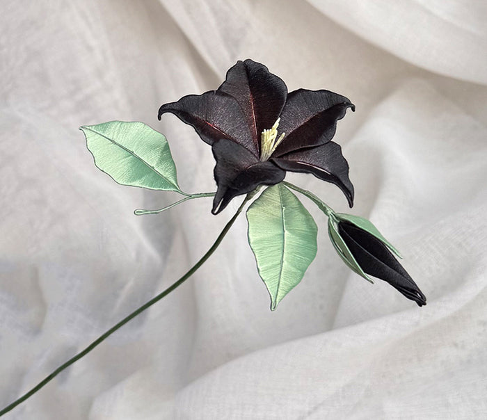 Handcrafted black Chanhua datura flower in a vase, showcasing a single stem with green leaves.