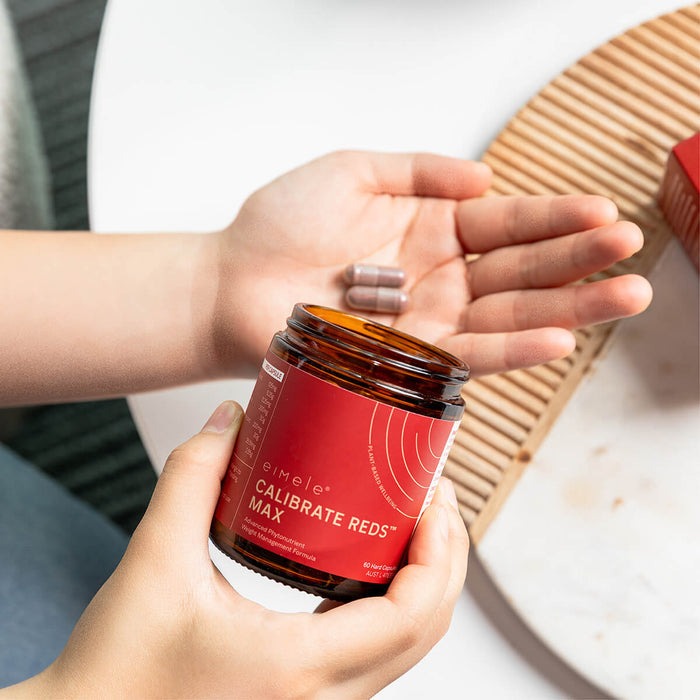 Hand holding eimele Calibrate Reds Max jar and capsules.