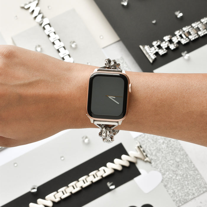 Close-up of the Chain Bracelet Apple Watch Strap - Silver by Coconut Lane on a person's wrist. The background features various stylish watch bands and metallic decorative elements, adding a sophisticated and modern aesthetic to the scene.