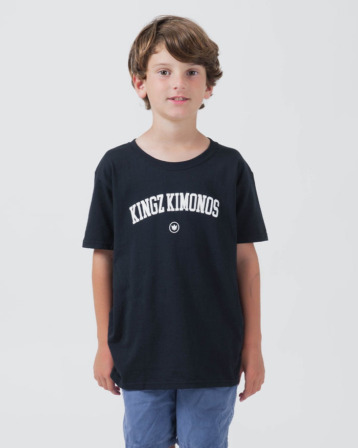 Kingz Collegiate Youth Tee Black - Front View Young Male Athlete Black Tee White KINGZ KIMONOS Text Center Small Crown Badge Streetwear Casual Apparel [color:Black]