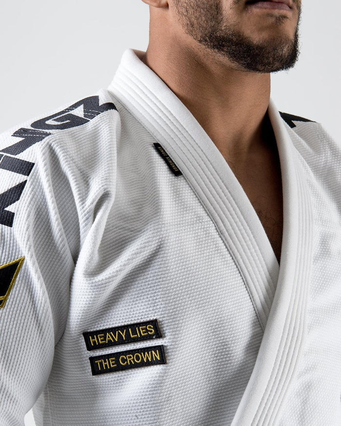 Kingz Comp 450 V6 Gi - White - Close-Up Detail View Male Athlete Shoulder KINGZ Text Black Patch "HEAVY LIES THE CROWN" White Fabric Texture Premium BJJ Kimono Jiu Jitsu Gear [color:White]