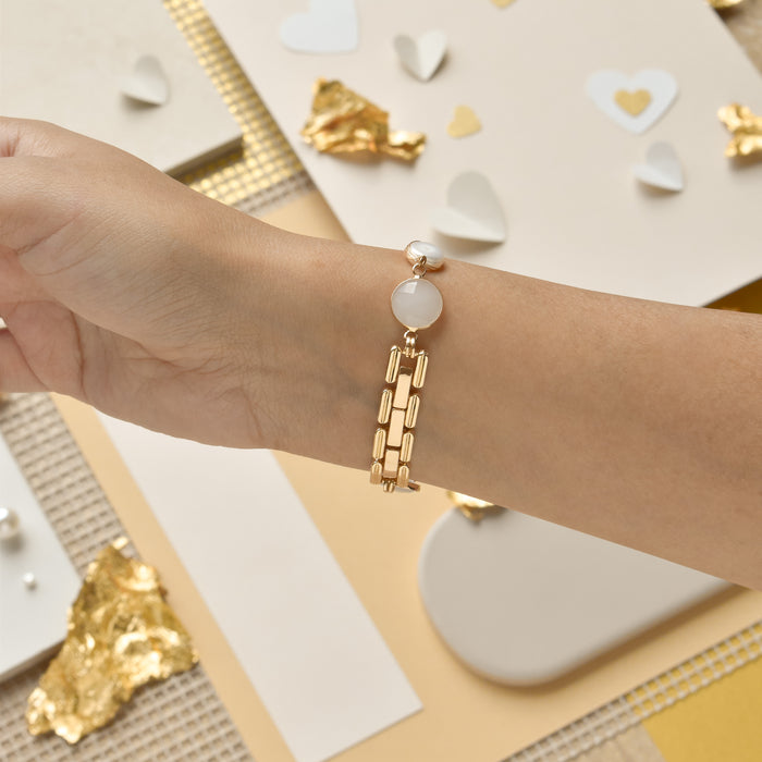 A close-up of a wrist adorned with Coconut Lane's Cute Stone Bracelet Apple Watch Strap, featuring a white gemstone charm. The background includes various decorative items such as paper hearts, gold foil pieces, and neutral-toned paper, creating a stylish and elegant setting.