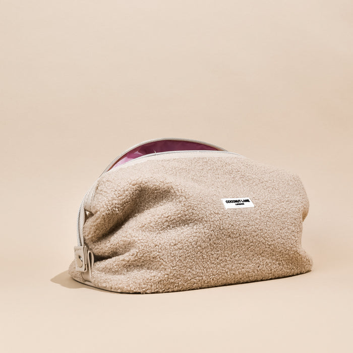 Beige sherpa expandable makeup bag with zip and small white label, shown on a neutral background.